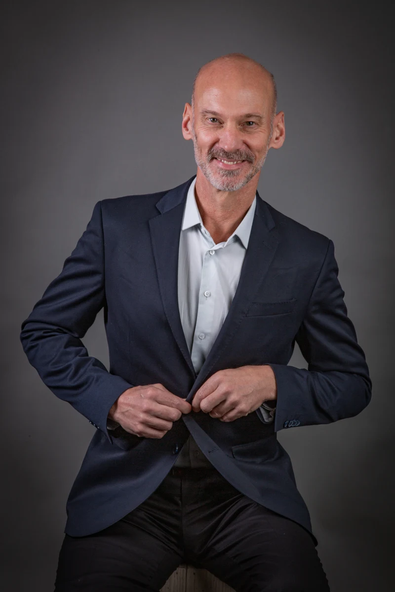 Retrato masculino con traje azul y manos juntas.