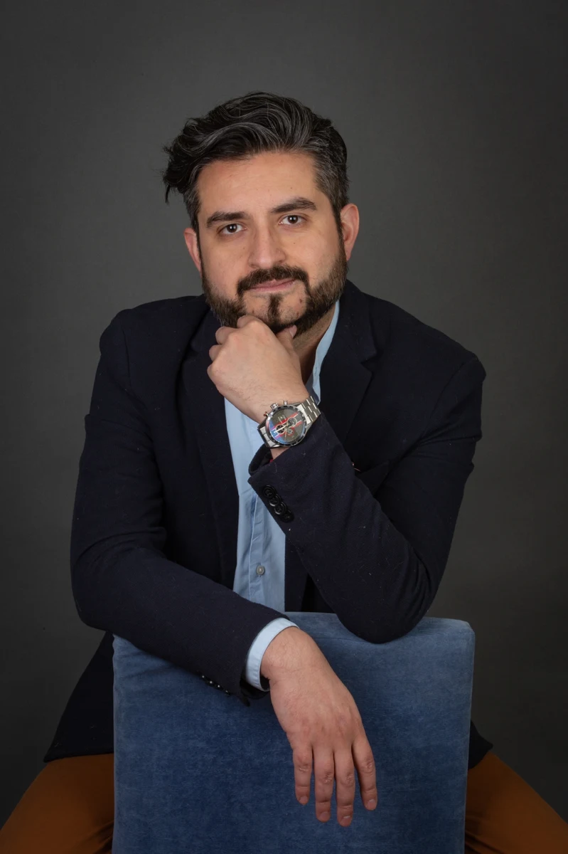 Retrato masculino con traje negro y mano en el rostro.
