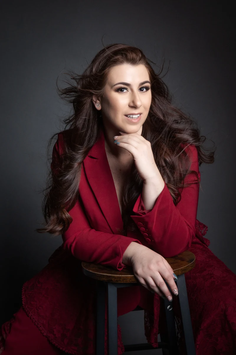 Retrato sentado con chaqueta roja y fondo oscuro.